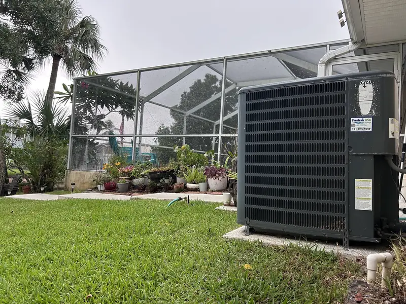 Condenser beside a screened lanai and lawn